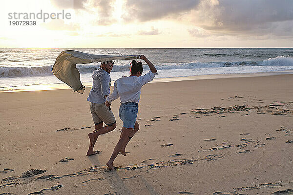 Fröhliches Paar läuft gemeinsam im Sand am Strand