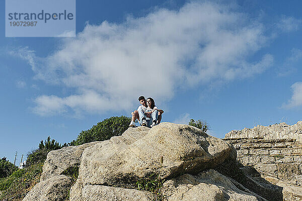Junges Paar sitzt auf Felsen unter dem Himmel