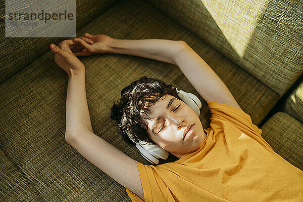 Teenage boy wearing headphones lying on sofa