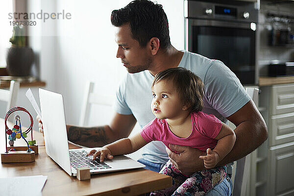 Vater mit kleinem Mädchen benutzt Laptop auf Tisch zu Hause