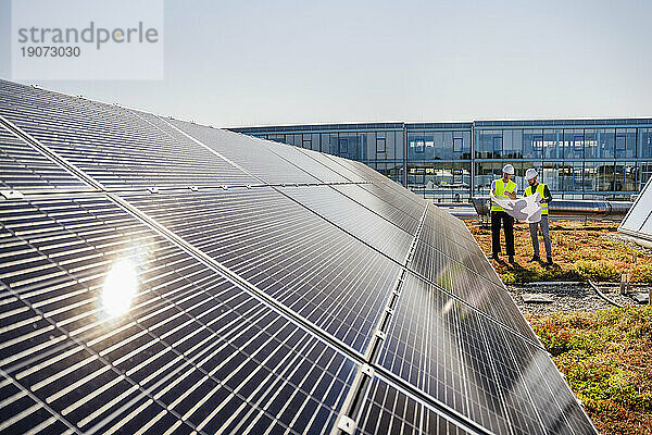 Zwei Techniker studieren den Plan auf dem Dach eines Firmengebäudes mit Solarpaneelen