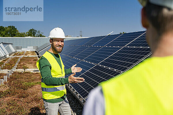 Techniker im Gespräch mit Kollegen auf dem Dach eines Firmengebäudes mit Solarpaneelen