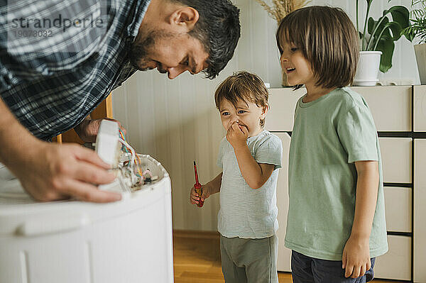 Glückliche Kinder  die zuschauen  wie der Vater zu Hause die Waschmaschine repariert