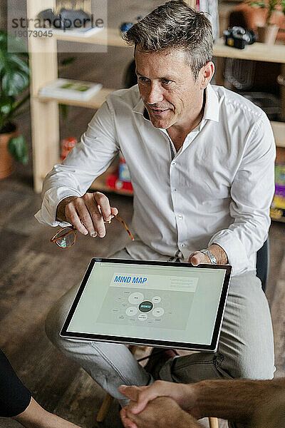 Geschäftsmann erklärt während einer Präsentation im Loft-Büro eine Mindmap auf dem Tablet-Bildschirm