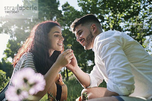 Smiling woman giving flower to boyfriend at park