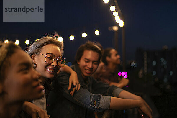 Lächelnde Freunde genießen es nachts auf dem Dach