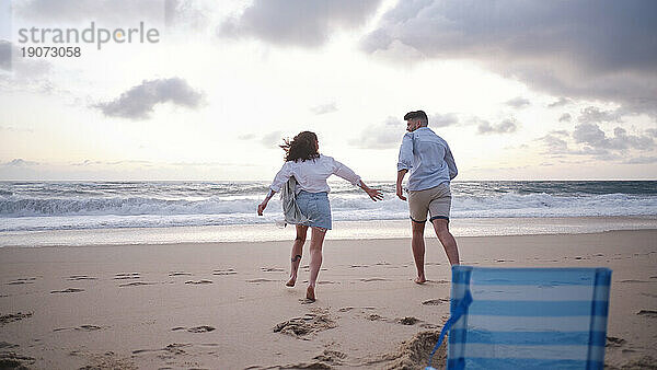 Junges Paar rennt am Strand in Richtung Meer