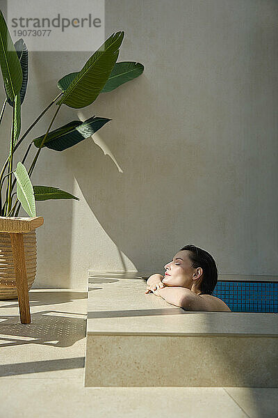 Young woman with eyes closed resting in hot tub at spa