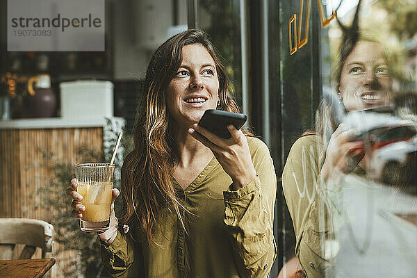 Glückliche junge Frau  die im Café mit dem Smartphone spricht