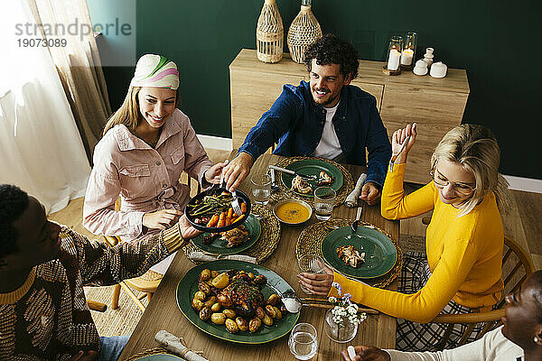 Lächelnde Freunde genießen das Mittagessen am Esstisch zu Hause