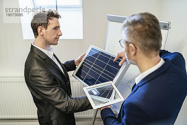 Zwei Geschäftsleute im Büro mit Solarzelle und Tablet diskutieren