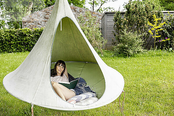 Entspannte Frau liest Buch in einem hängenden Zelt