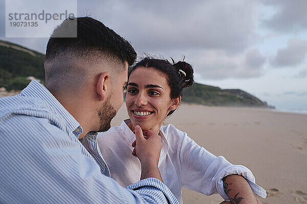 Man touching girlfriend's chin sitting at beach
