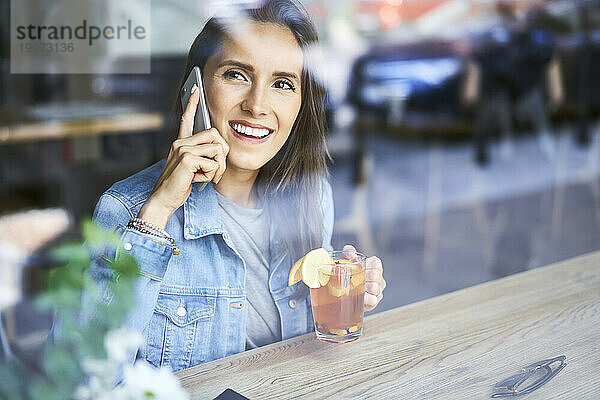 Lächelnde junge Frau am Telefon  die im Café Tee trinkt