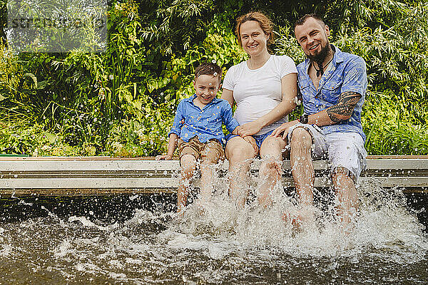 Glückliche schwangere Mutter mit Familie  die auf der Fußgängerbrücke über den See Wasser spritzt