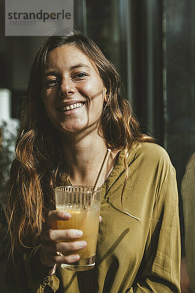 Lächelnde junge Frau hält ein Glas Saft