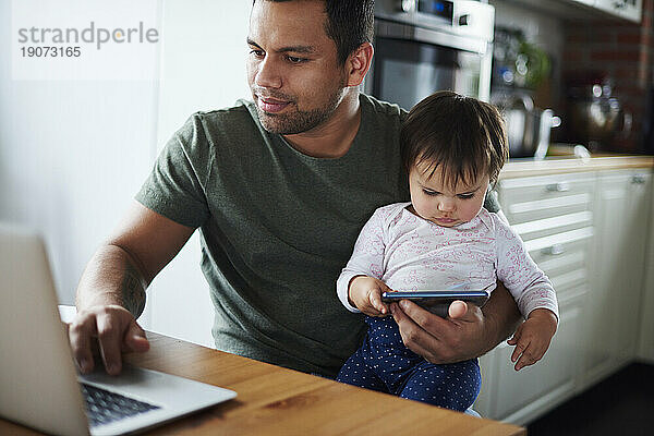 Vater nutzt Laptop und kleines Mädchen nutzt Smartphone zu Hause