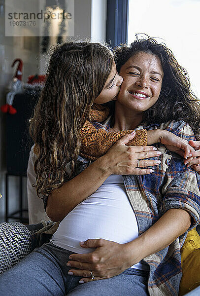 Mädchen küsst glückliche schwangere Mutter im Wohnzimmer