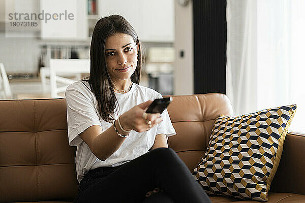 Young woman sitting on couch at home watching Tv