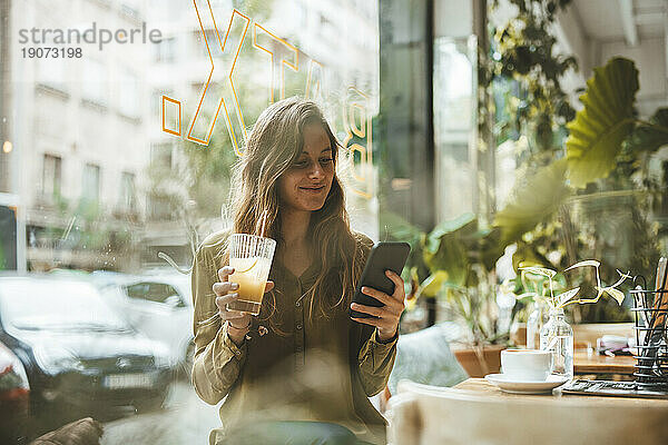 Lächelnde junge Frau mit Saft und Smartphone im Café