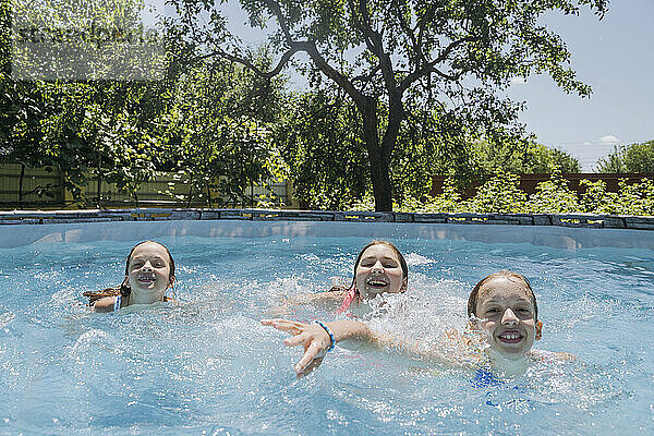 Smiling friends splashing water in pool at summer