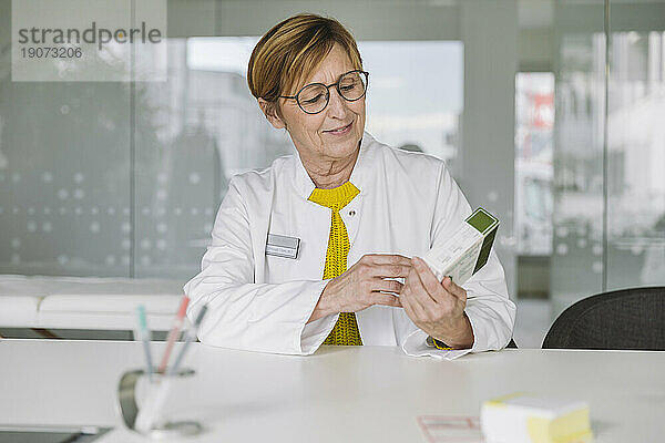 Arzt sitzt am Schreibtisch und hält Medikamente in der Hand
