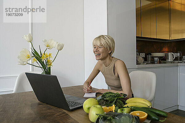 Lächelnder Ernährungsberater macht sich zu Hause vom Laptop aus Notizen über die Ernährung