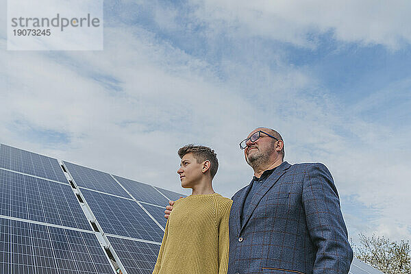 Nachdenklicher Vater und Sohn stehen neben einem Solarpanel unter dem Himmel