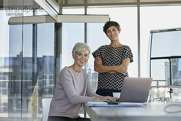 Porträt zweier lächelnder Geschäftsfrauen mit Laptop am Schreibtisch im Büro