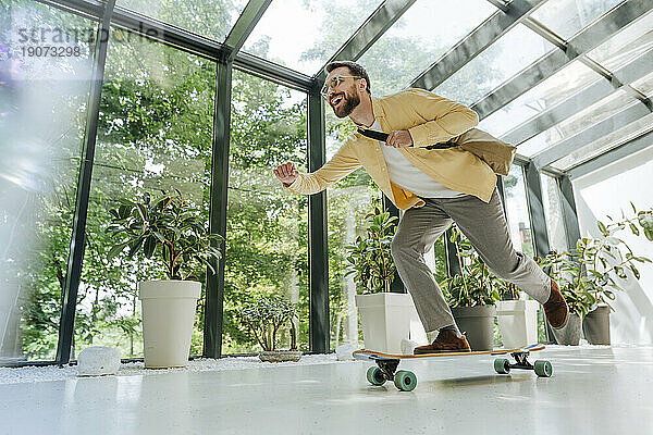 Fröhlicher Geschäftsmann genießt Longboard-Skaten im Büro