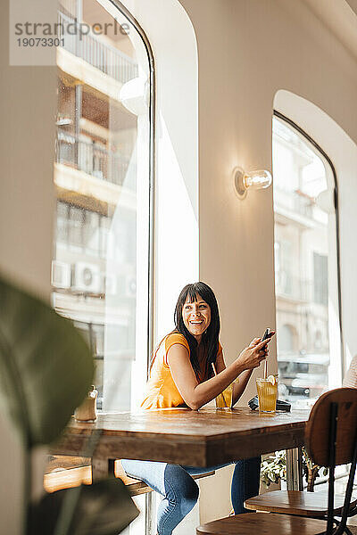 Glückliche reife Frau mit Smartphone sitzt im Café