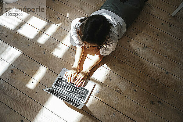 Freiberufler arbeitet mit Laptop  der zu Hause auf dem Hartholzboden liegt