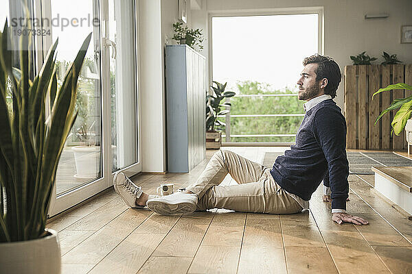 Young man sitting on floor  looking out of window  relaxing