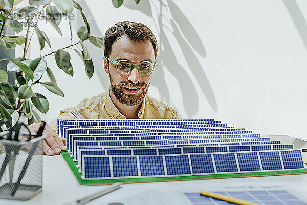 Lächelnder Geschäftsmann untersucht Solarpanel-Modell im Büro