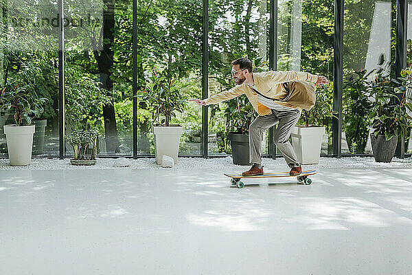 Glücklicher Geschäftsmann beim Longboard-Skaten vor Pflanzen