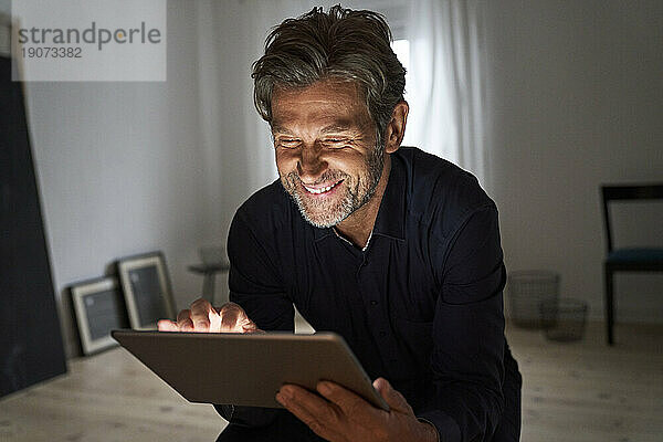 Porträt eines lächelnden reifen Mannes  der zu Hause Spaß mit einem digitalen Tablet hat