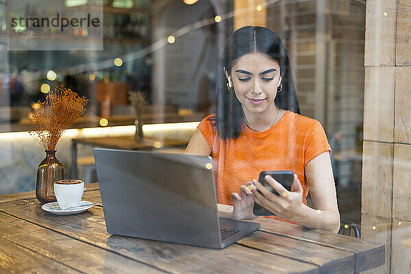 Lächelnder Freiberufler nutzt Smartphone im Café