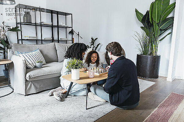 Eltern sitzen im Wohnzimmer und bringen ihrer Tochter das Schachspielen bei