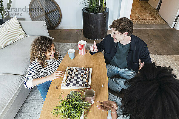 Eltern sitzen im Wohnzimmer und bringen ihrer Tochter das Schachspielen bei