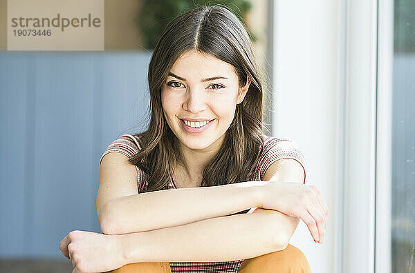Portrait of smiling young woman sitting at the window at home