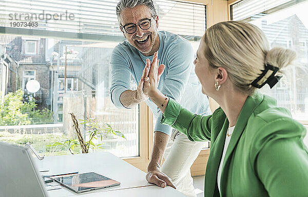 Fröhlicher Geschäftsmann  der einer Geschäftsfrau im Büro High-Five gibt