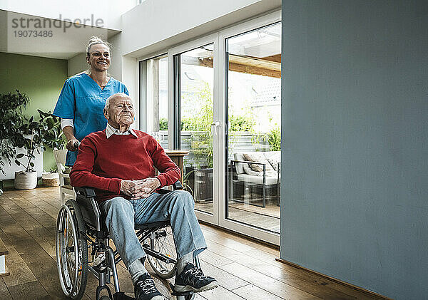 Glückliche Krankenschwester  die sich um einen älteren Mann kümmert  der zu Hause im Rollstuhl sitzt