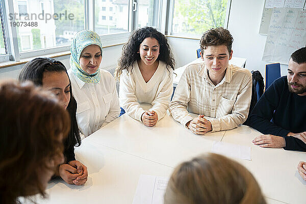 Schüler sitzen mit gefalteten Händen um den Tisch im Klassenzimmer