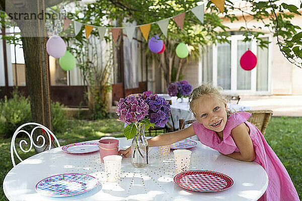 Lächelndes Mädchen deckt Tisch für Geburtstagsveranstaltung im Garten