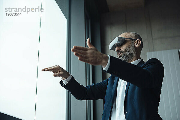 Reifer Geschäftsmann gestikuliert mit Virtual-Reality-Simulatoren im Büro