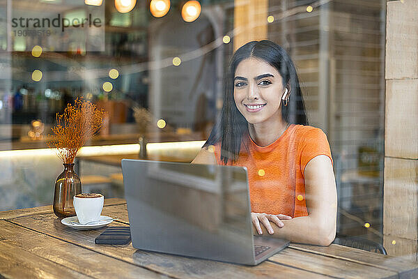 Lächelnder Freiberufler sitzt mit Laptop im Café