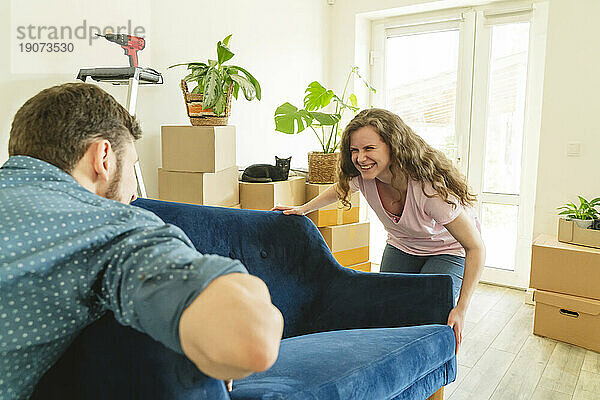 Happy woman helping boyfriend to carry sofa in new home