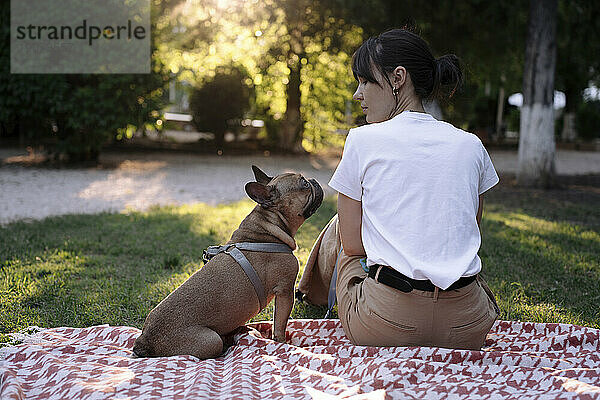 Frau schaut Hund an  der auf Decke im Park sitzt