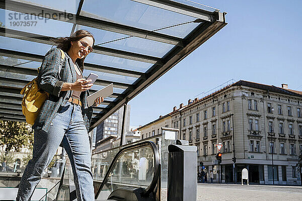 Lächelnde Frau benutzt Smartphone und geht auf der Straße