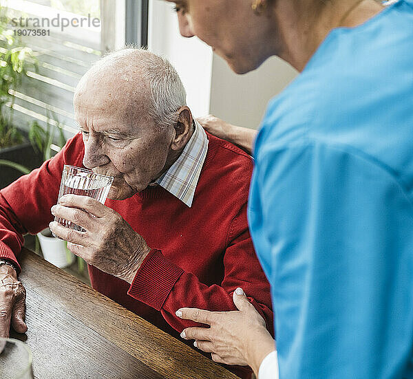 Krankenschwester kümmert sich um Trinkwasser des älteren Mannes am Tisch